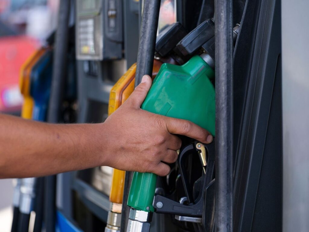 Hand holding a green fuel nozzle at a service station pump