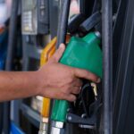 Hand holding a green fuel nozzle at a service station pump
